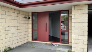 A building entrance with a red door and glass panels, a brick wall, and a small step leading to the door.