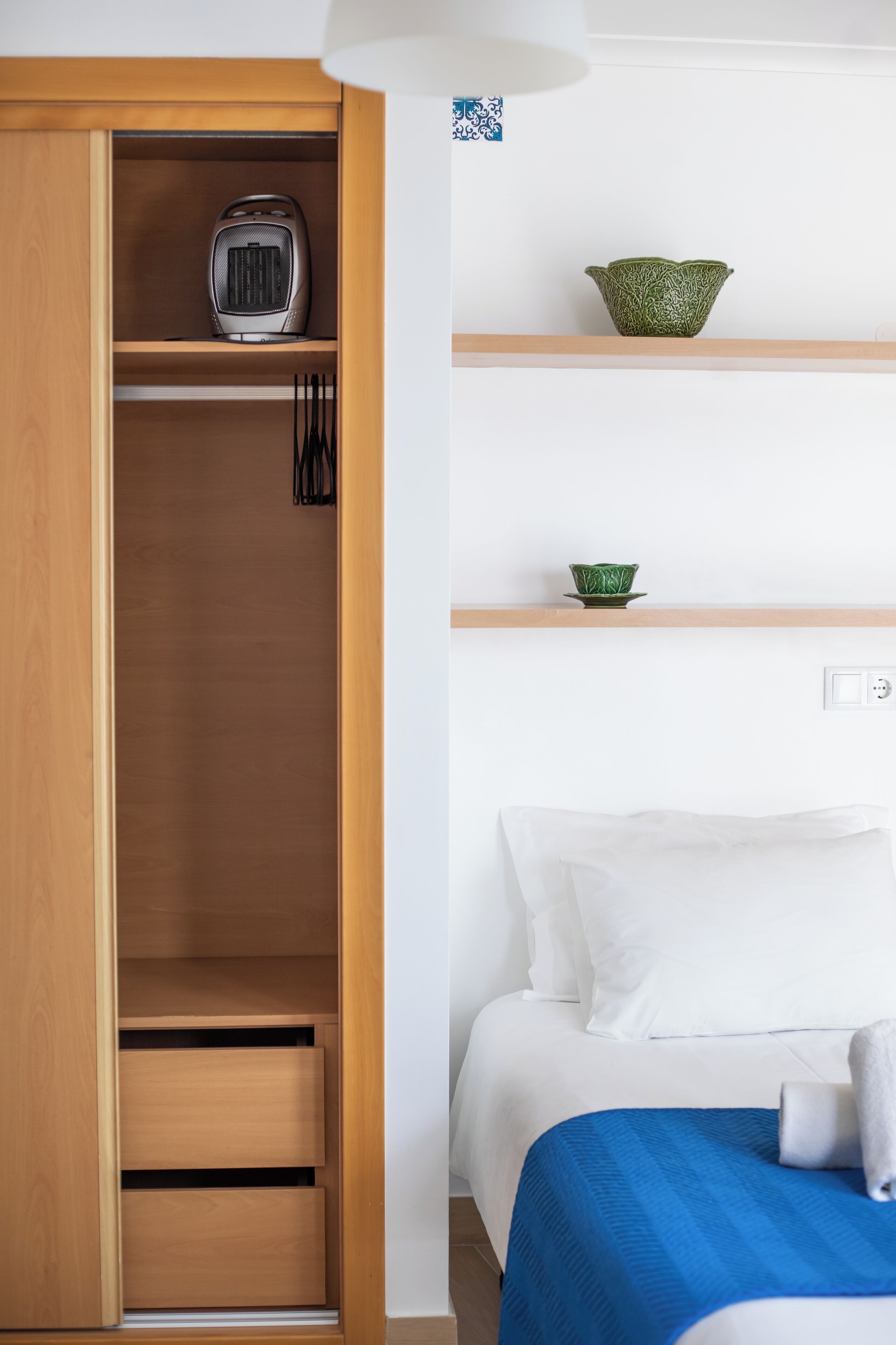 Un dormitorio con un armario de madera, una cama con ropa de cama blanca y un tazón verde sobre una estantería.