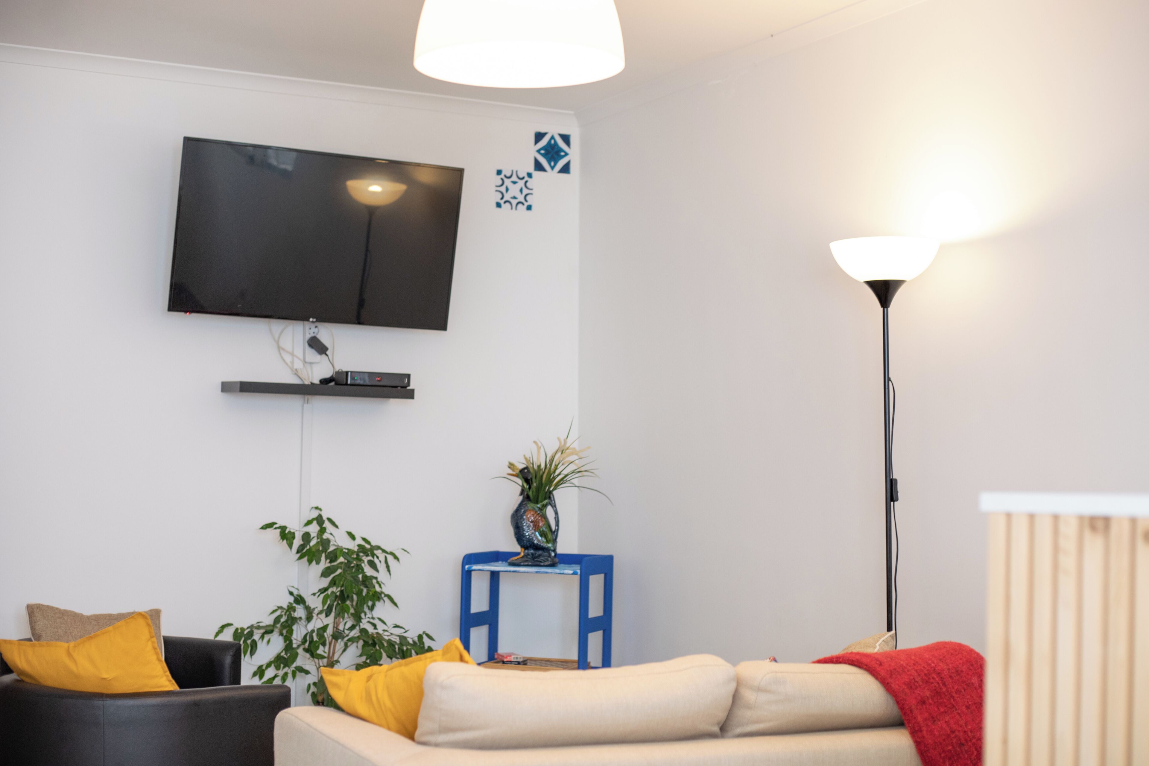 Un soggiorno moderno con una TV a schermo piatto montata a parete, un tavolino blu con una pianta, un divano con cuscini gialli e una coperta rossa.