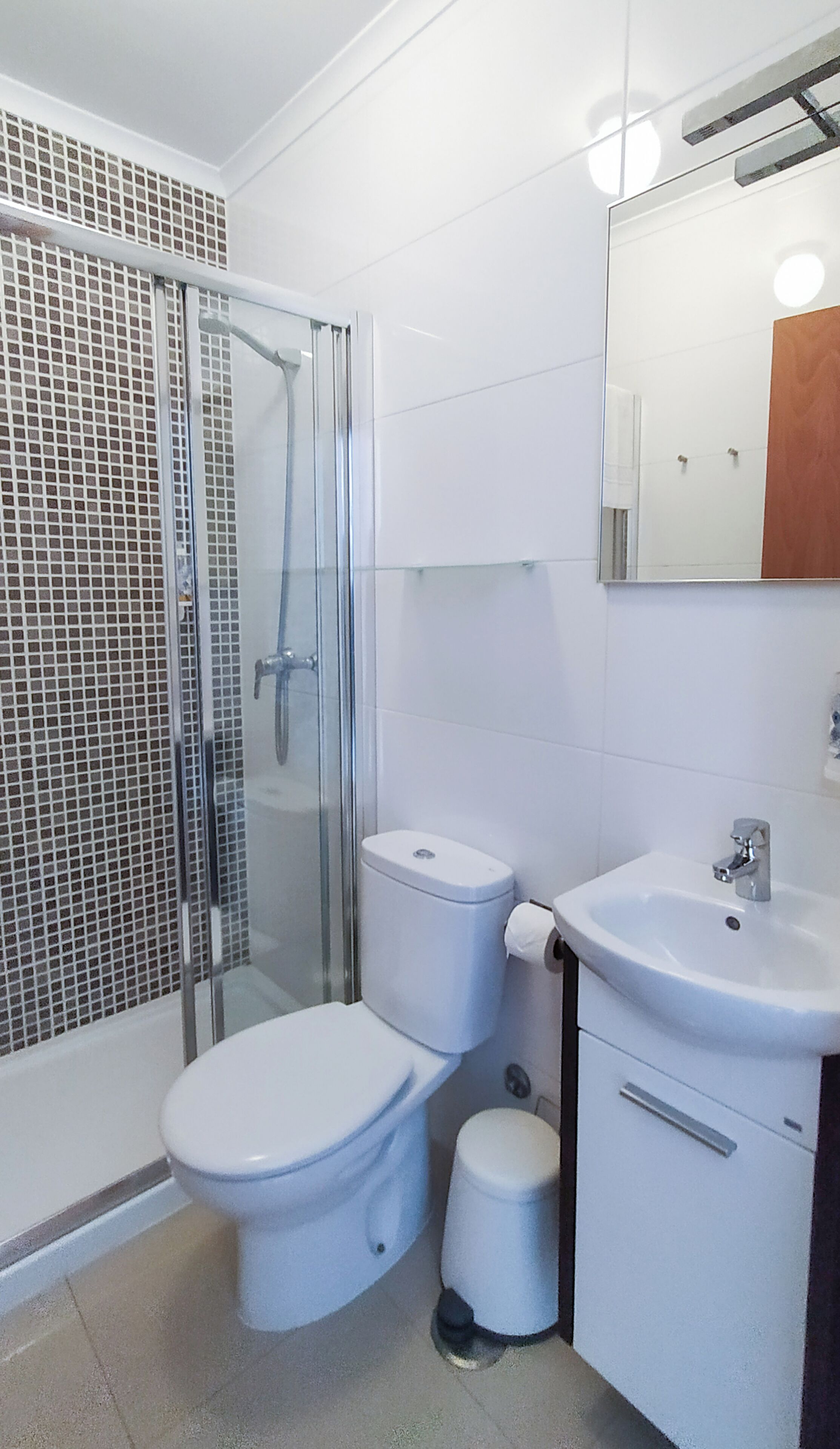 Un baño con ducha envuelta en vidrio, dos inodoros, un lavamanos y un espejo.