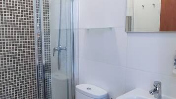 Un baño con ducha envuelta en vidrio, dos inodoros, un lavamanos y un espejo.