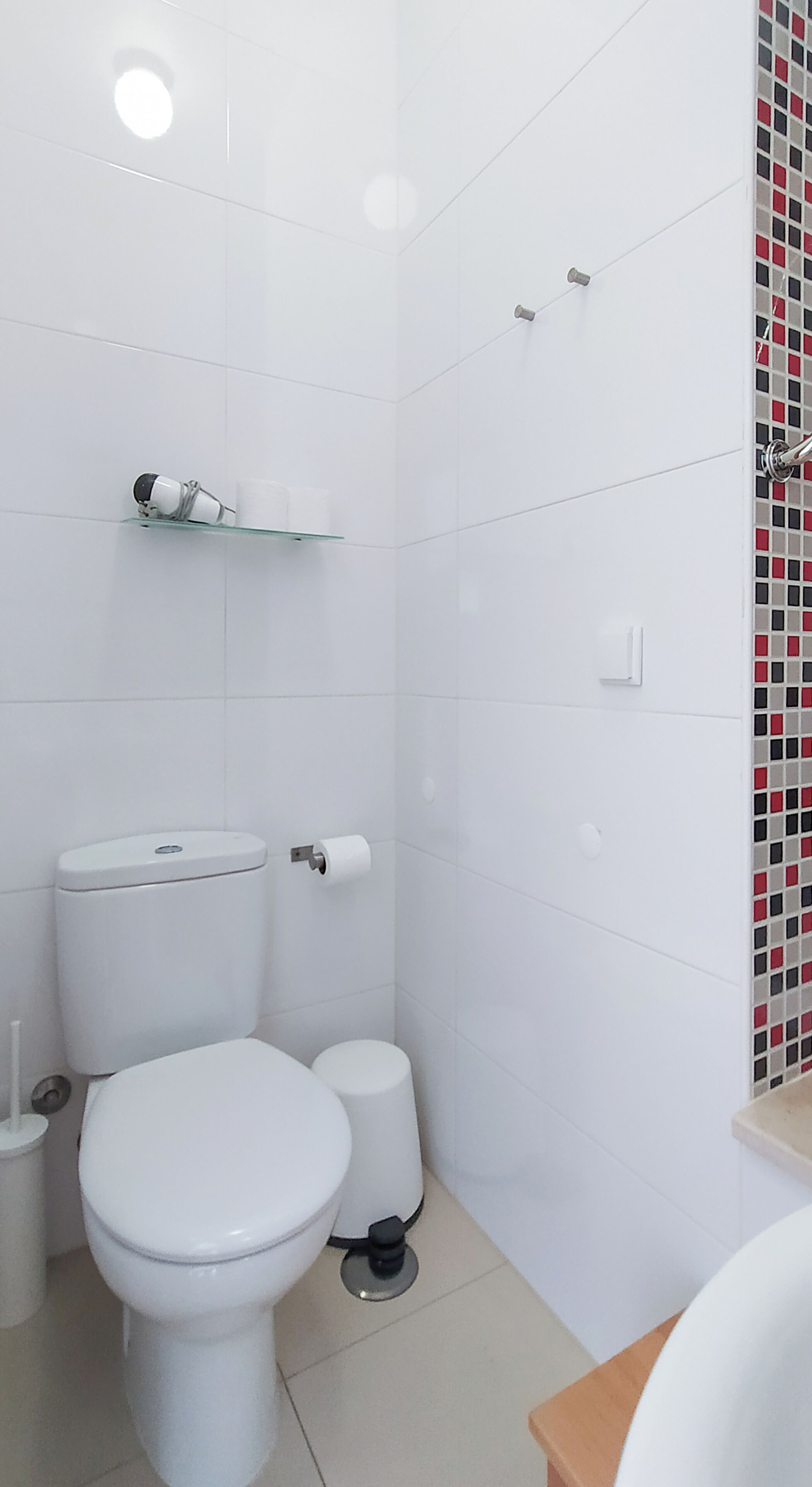 Un baño con inodoro, bidé y un estante con una cámara y tazas.
