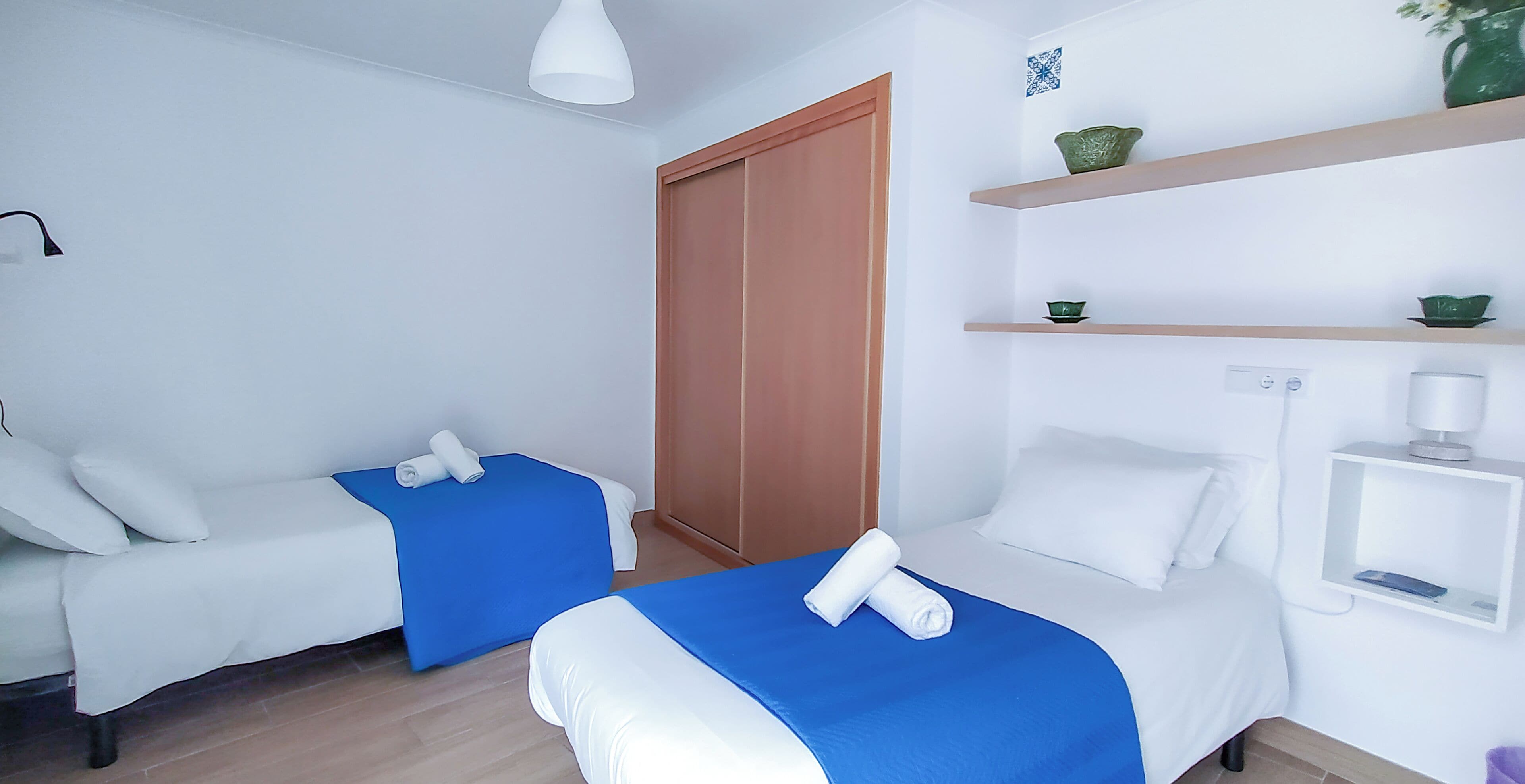Een hotelkamer met twee bedden, een garderobe, een plank met decoratieve spullen en een nachtkastje met een lamp.