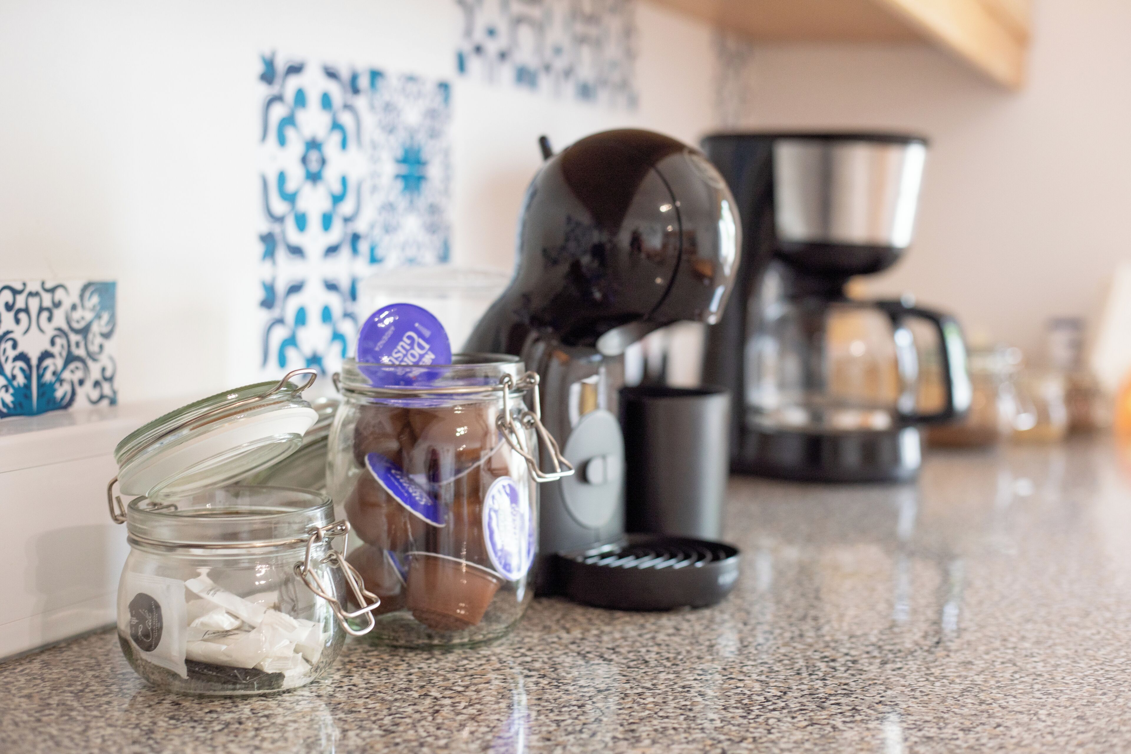 A kitchen counter with a coffee maker, a jar of chocolate, and a spice rack.