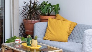 Una habitación con un sofá gris, un cojín amarillo y varias plantas en macetas.