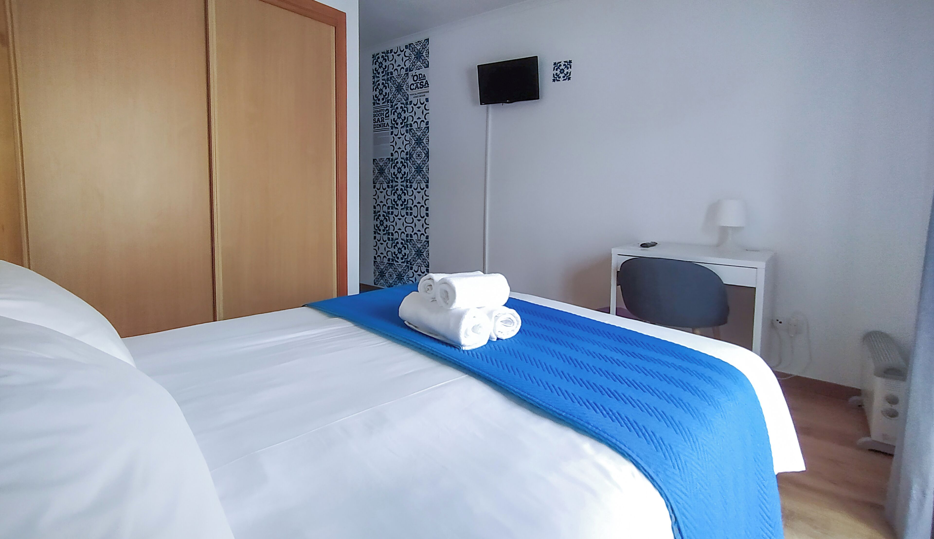 Una habitación de hotel con cama, armario, televisor montado en la pared y escritorio con silla.