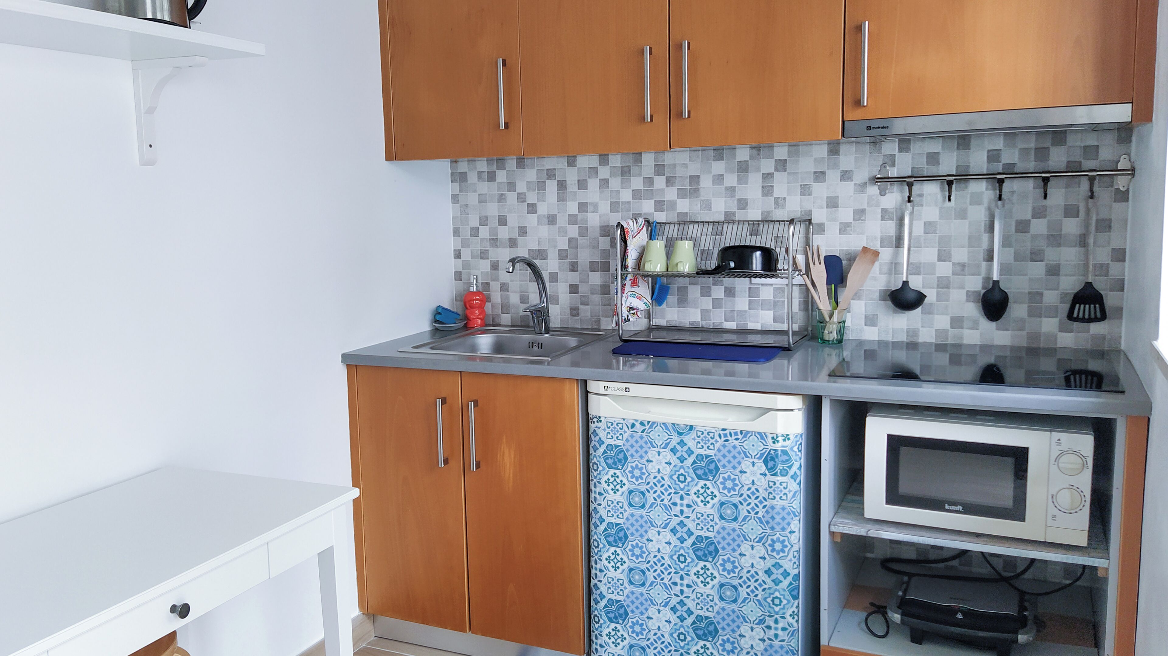 A compact kitchen with wooden cabinets, a dishwasher, a microwave, and a tiled backsplash.