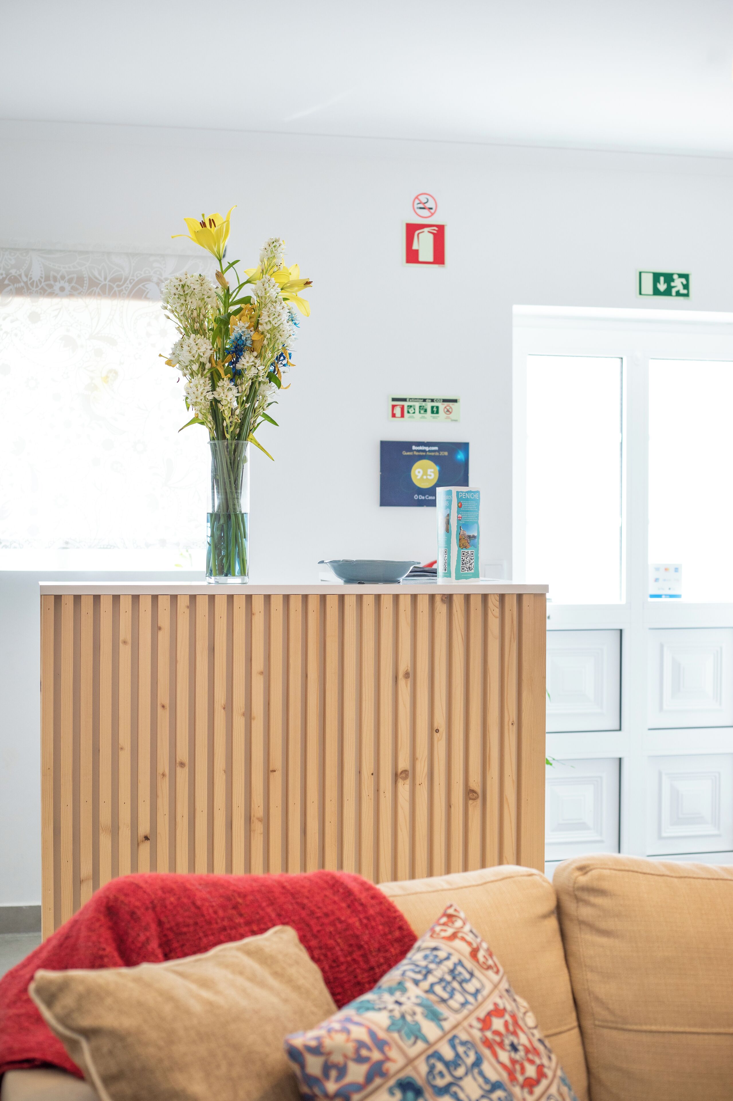 A reception area with a wooden counter, a vase of flowers, a fire safety sign, and a door with an exit sign.