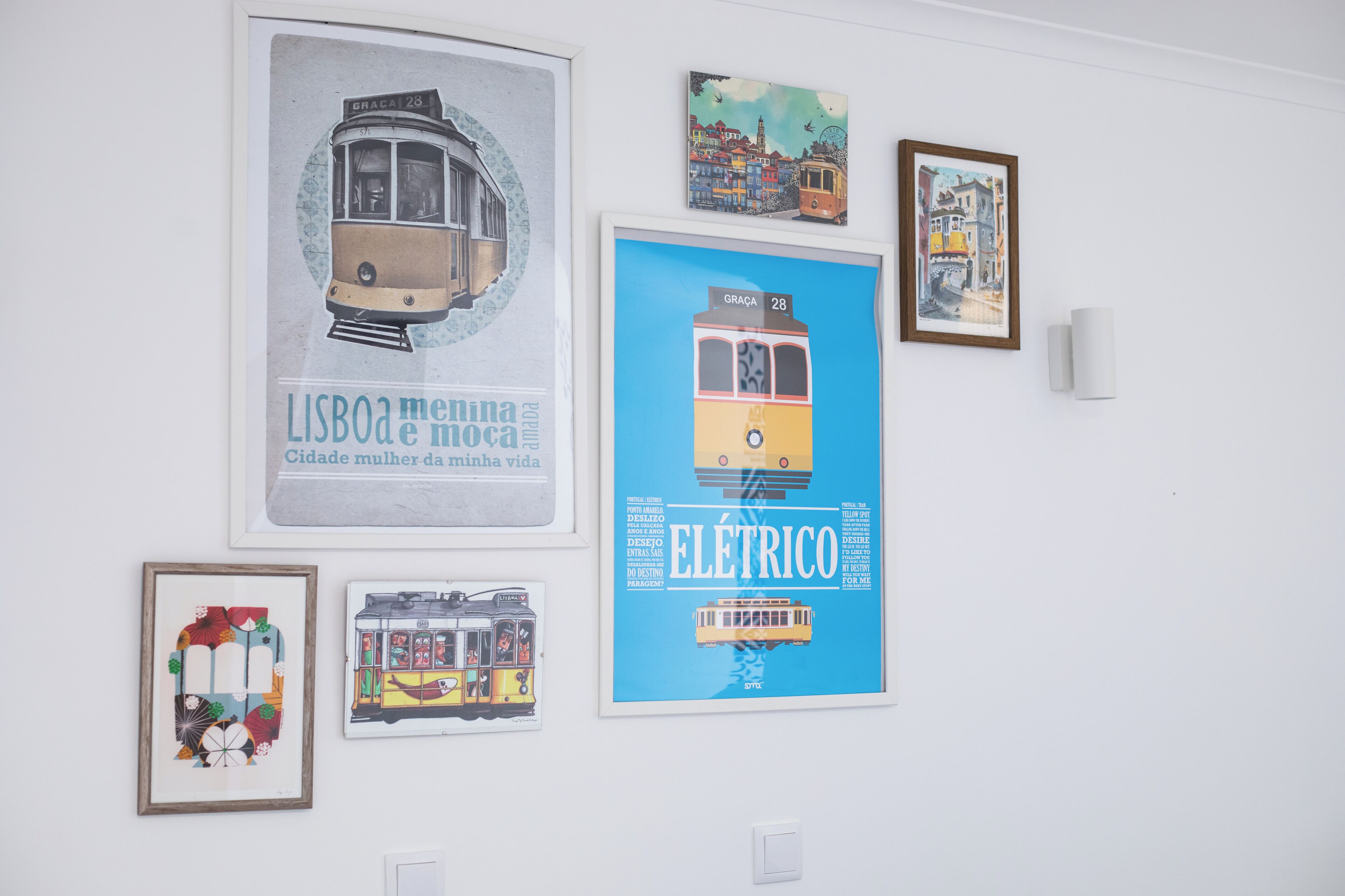 A wall with various framed artworks, including posters of trams and a cityscape.