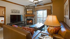 A living room with a stone fireplace, a television, a ceiling fan, and a large window. - Rare 1BR for 4 at Westgate Park City. Ski-In/Ski-Out. Walk to Gondola. (Park City)
