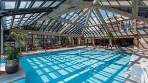 A large indoor swimming pool with a glass ceiling, surrounded by lounge areas and potted plants. - Rare 1BR for 4 at Westgate Park City. Ski-In/Ski-Out. Walk to Gondola. (Park City)