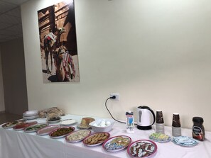 A buffet table with various food items and beverages, a wall-mounted artwork, and a power outlet. - Rakan Apartment (Wadi Musa)