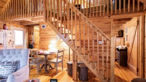 A cozy cabin interior with a wooden staircase, a dining area, and a living room with a sofa and a table. - Shaded Log Cabin Swim Spa 2 miles Lake Entrance & winery (Birdseye)