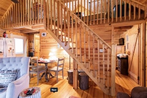 L’intérieur d’un chalet accueillant, avec un escalier en bois, un coin repas et un salon comprenant un canapé et une table.