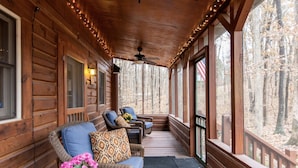 A wooden log cabin with a porch, furnished with wicker chairs and a sofa, and a view of a forest. - Shaded Log Cabin Swim Spa 2 miles Lake Entrance & winery (Birdseye)