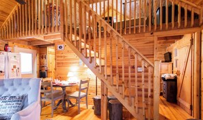 Interior acolhedor de cabana com escada de madeira, área de jantar e sala de estar com sofá e mesa.