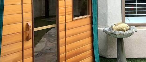 Un edificio de madera con un toldo verde, una pequeña fuente de piedra y una ventana con persianas.