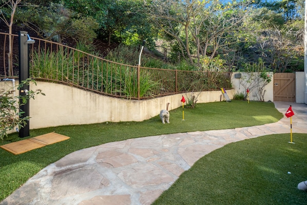 A stone pathway leading to a grassy area with a metal fence and trees in the background.