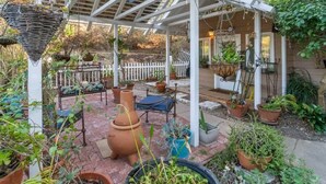 En overdækket terrasse med plantekasser, siddepladser og et hvidt hegn i baggrunden.