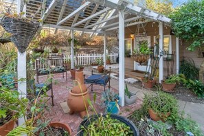 Un patio cubierto con plantas en macetas, una zona de estar y una valla blanca al fondo.