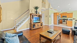 Un vaste salon doté d’un meuble de rangement en bois pour les appareils multimédias, d’un grand téléviseur et d’un escalier menant à l’étage supérieur.