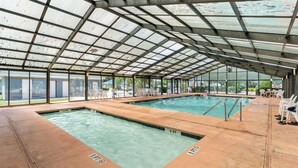 Une piscine intérieure à l’eau claire, entourée de chaises longues et dotée d’une structure de toit abritée.