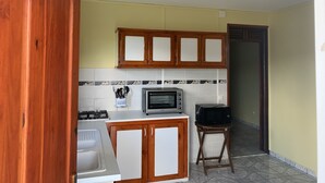 Cuina compacta amb armaris de fusta, fogó a gas, microones i una taula petita.
