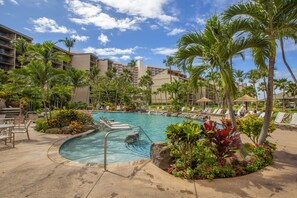 A hotel pool area with lounge chairs, palm trees, and a clear blue sky.
