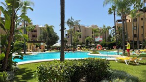 Area piscina con sedie a sdraio, palme e un edificio sullo sfondo.