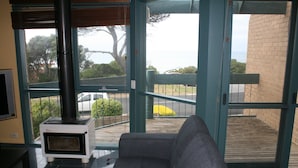 A living room with a gray sofa, a white wood-burning stove, and a view of the outdoors through large glass doors.