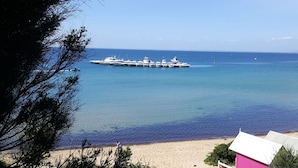 A beach with a row of yachts docked in the water, a sandy shore, and a building with a pink roof.