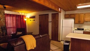 Una sala de estar acogedora con un sofá de cuero y una zona de cocina con armarios de madera y un refrigerador blanco.