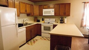 Una cocina compacta con armarios de madera, un refrigerador blanco, un microondas, un horno y una cafetera.