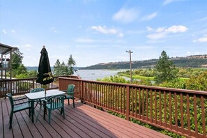 Une terrasse en bois avec une table et des chaises, donnant sur un lac et une végétation luxuriante.
