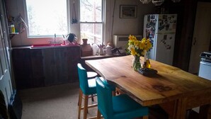 A kitchen with a wooden table, two blue chairs, a refrigerator, and a window with a view of trees. - Off Grid Mountain Farmhouse with amazing views, soaking tub, seclusion, internet (South Duxbury)