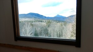 A room with a large window overlooking a forested landscape with mountains. - Off Grid Mountain Farmhouse with amazing views, soaking tub, seclusion, internet (South Duxbury)