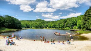 Una spiaggia sul lago con persone che si rilassano e nuotano, circondata da vegetazione lussureggiante.