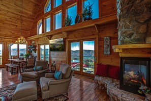 Un intérieur de chalet chaleureux avec une cheminée, de grandes fenêtres et un coin repas.