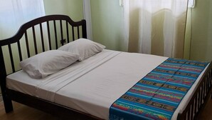 Una cama con ropa blanca y una colcha colorida, un cabecero de madera y un tapete a rayas en el suelo.