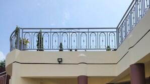 Un bâtiment à deux étages doté d’un balcon, d’un escalier menant à l’entrée et de deux grands pots de fleurs ornés de fleurs roses.