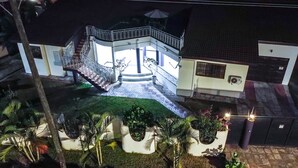 Une maison à deux étages dotée d’un balcon, d’un escalier et d’un petit jardin agrémenté de plantes en pot.