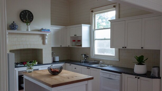 A kitchen with white cabinets, a wooden island, a sink, a dishwasher, and a window with a view.