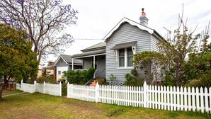 A two-story house with a white picket fence, a front porch, and a chimney.