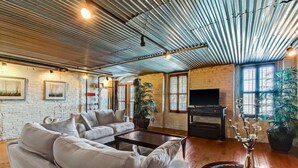 A spacious living room with a sectional sofa, a coffee table, and a TV. The room features exposed ceilings, brick walls, and large windows. - Amazing Loft with Balcony Overlooking River Street by Lucky Savannah (Savannah)