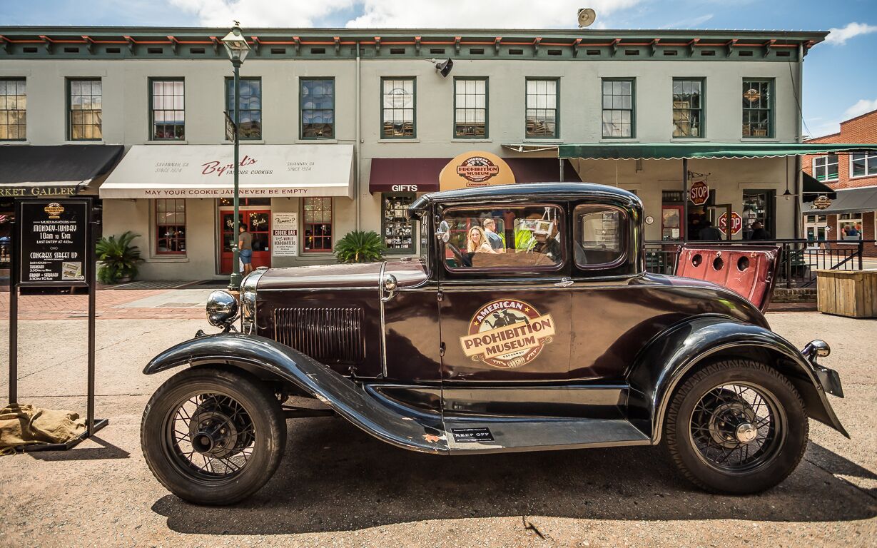 A vintage car parked in front of a building with a sign reading "American Prohibition Museum."