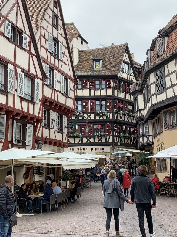 A cobblestone street lined with traditional half-timbered buildings, outdoor seating for cafes, and a sign reading "au vier pignon". - Historical town center spacious flat (Colmar)