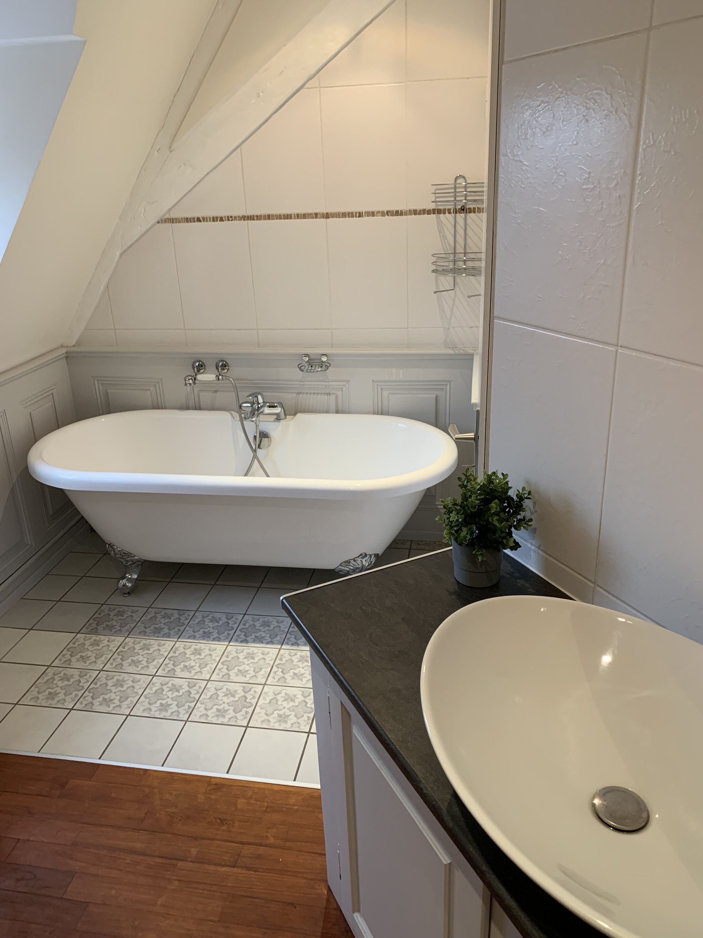 Un baño con bañera independiente, lavamanos y planta en maceta.