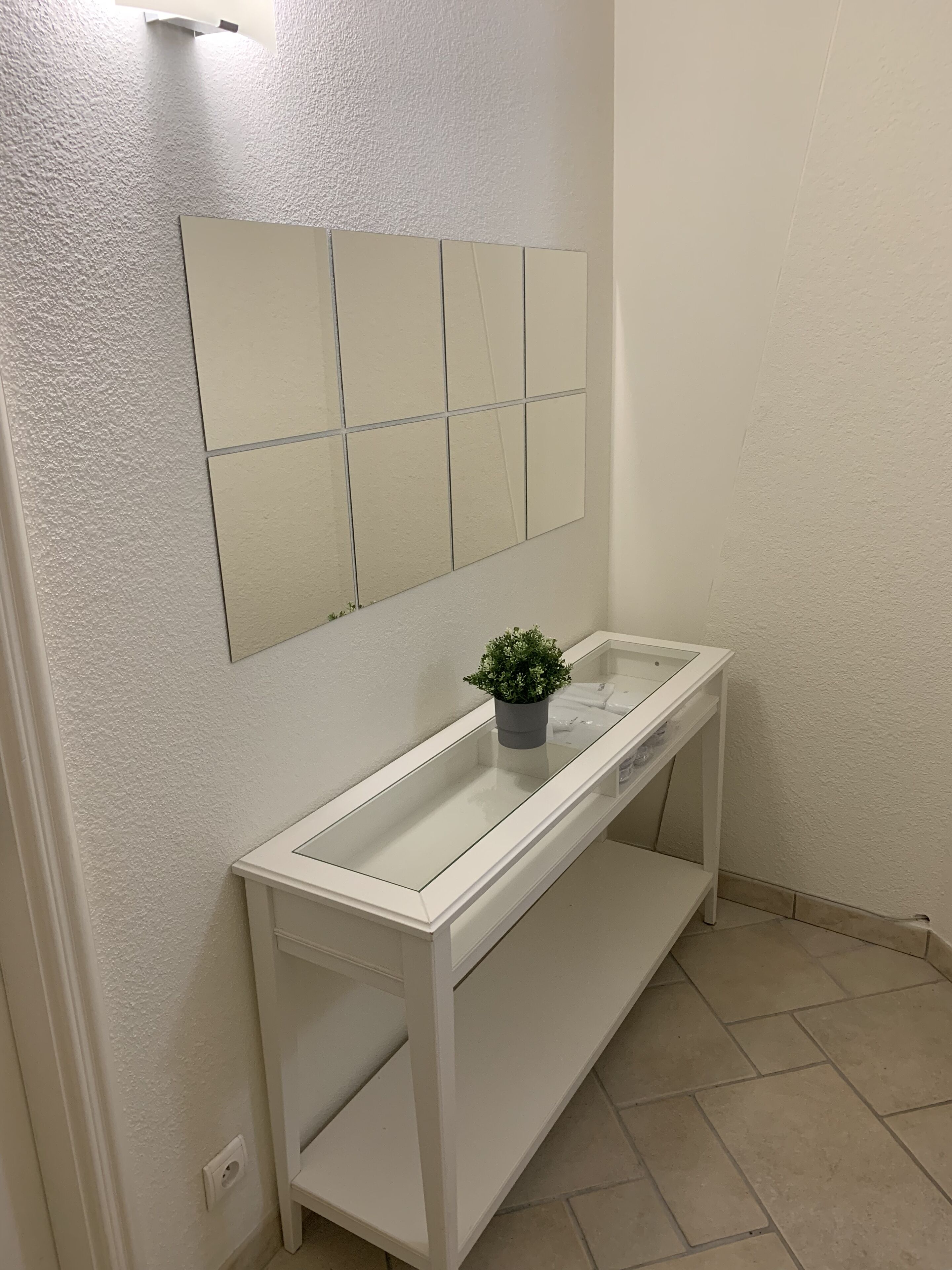 A white console table with a glass top, a potted plant, and a mirror above it.