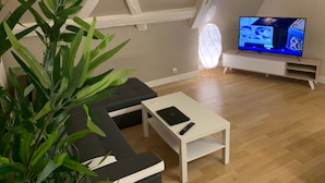 A modern living room with a black sectional sofa, a white coffee table, and a television on a white stand.