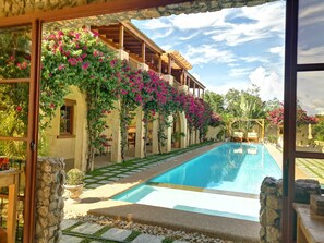 Un espace aménagé au bord d’une piscine à l’eau d’un bleu limpide, avec des marches en pierre menant à la piscine et un bâtiment orné de plantes grimpantes aux fleurs roses.